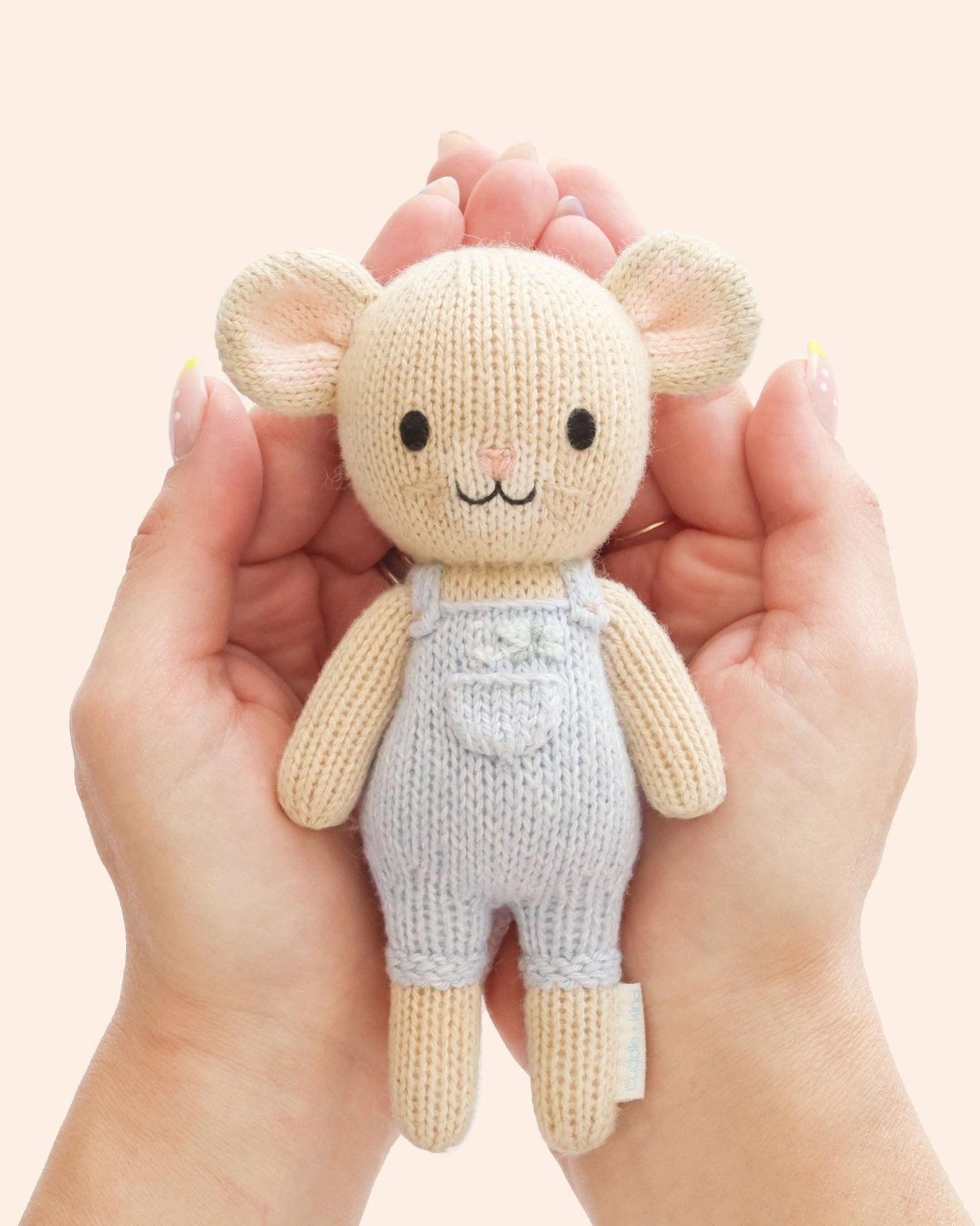 Knitted toy mouse held in hands against a light pink background