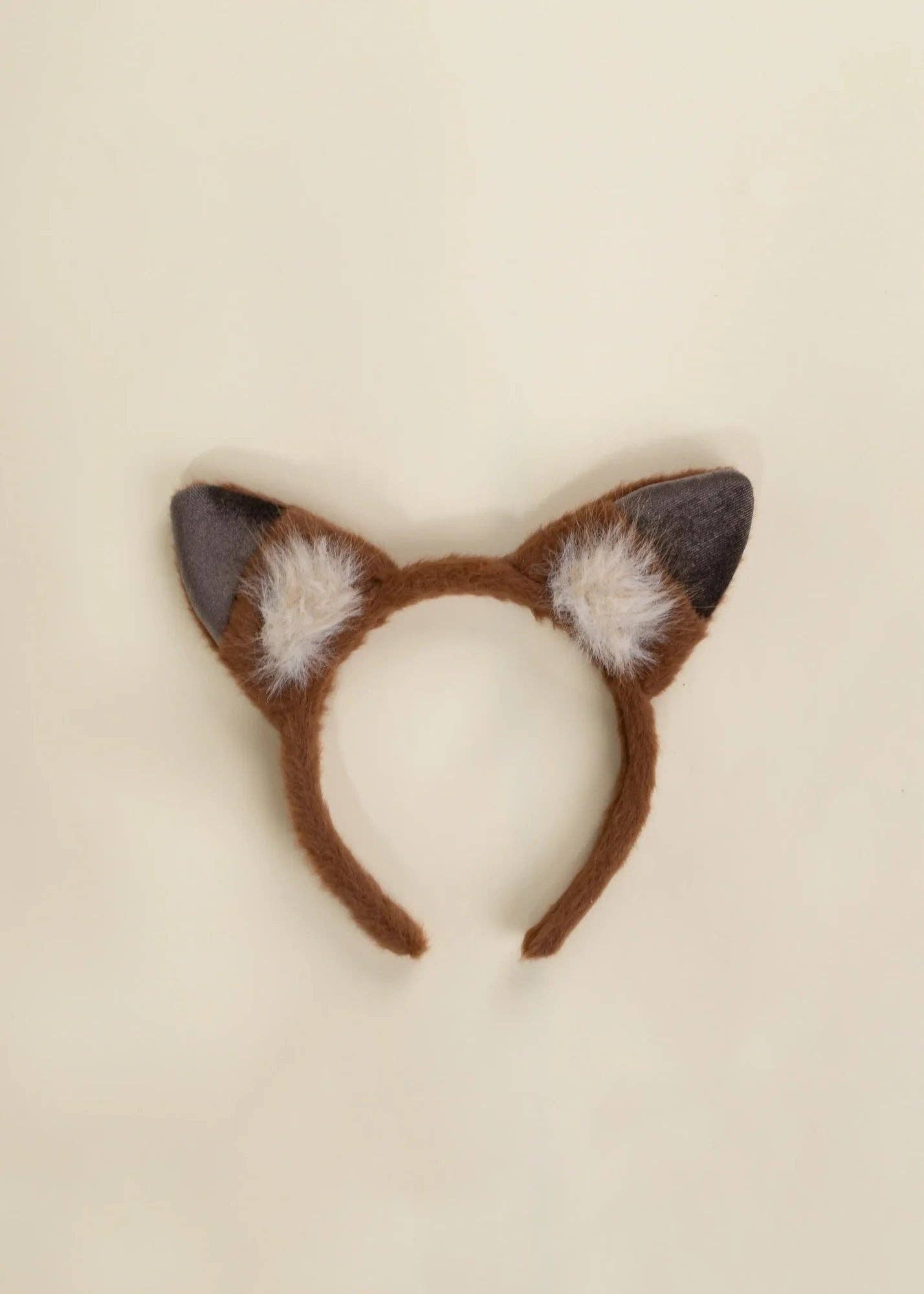 A brown faux-fur fox ears headband with dark gray inner ears and white fluffy accents, displayed on a light cream background.
