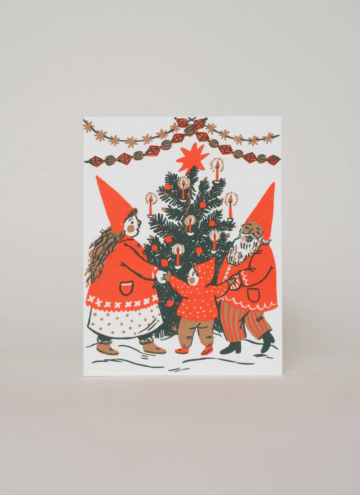 A holiday greeting card featuring a sweet gnome family dancing around the Christmas tree.