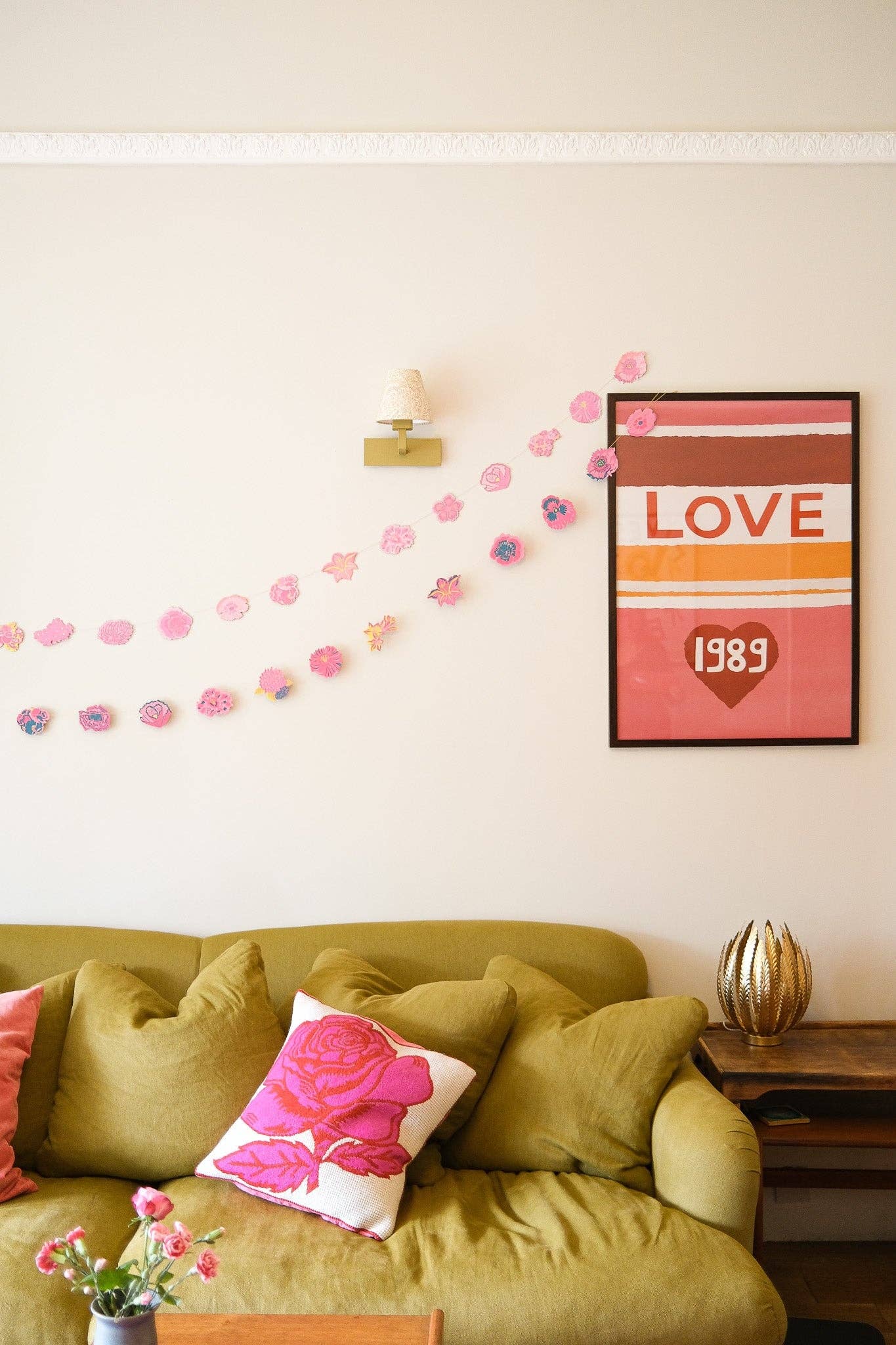 Living room with green sofa, decorative floral garland and pillows, and a 'LOVE 1989' wall art.