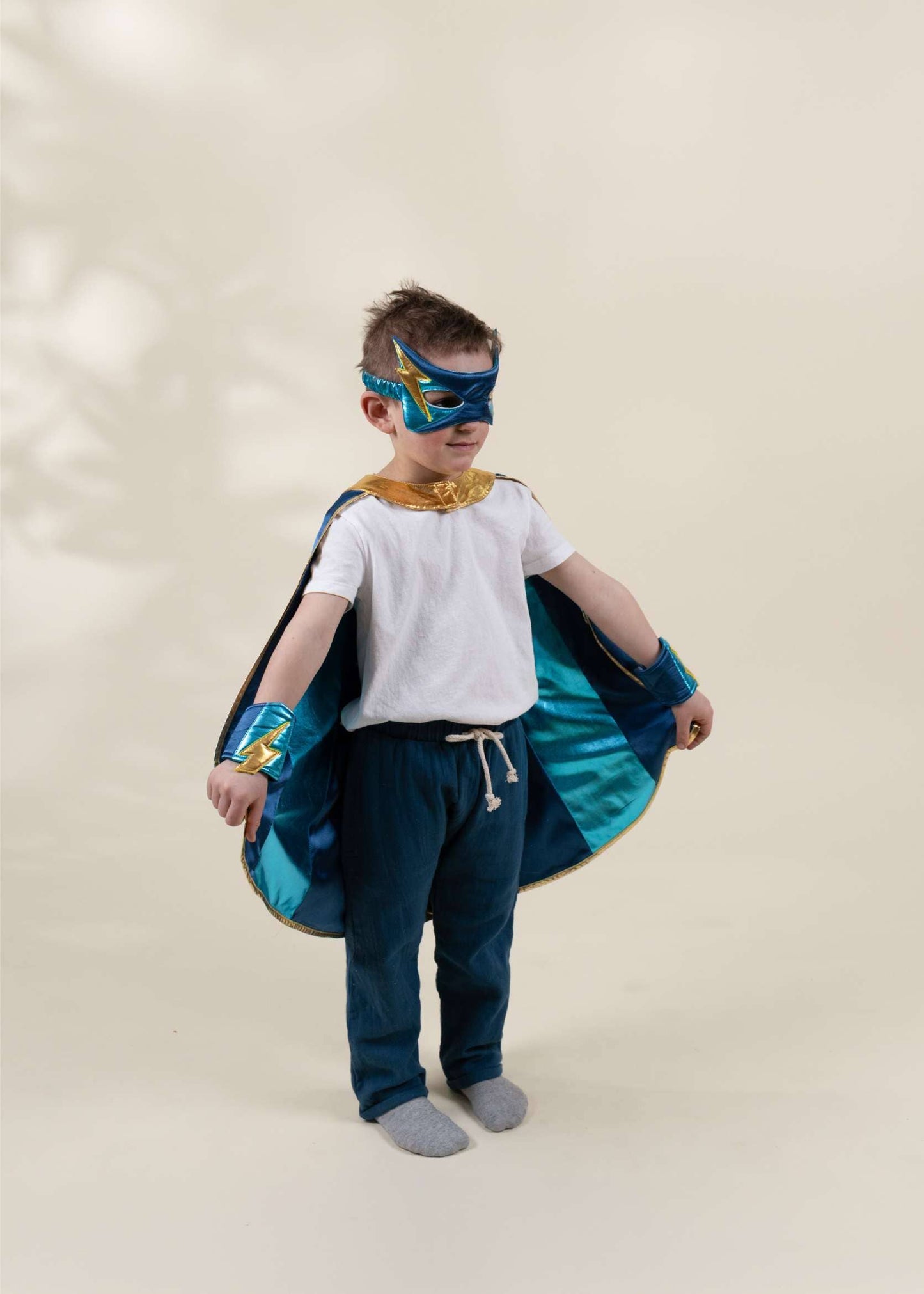 Child wearing a superhero costume with cape and mask on a plain background