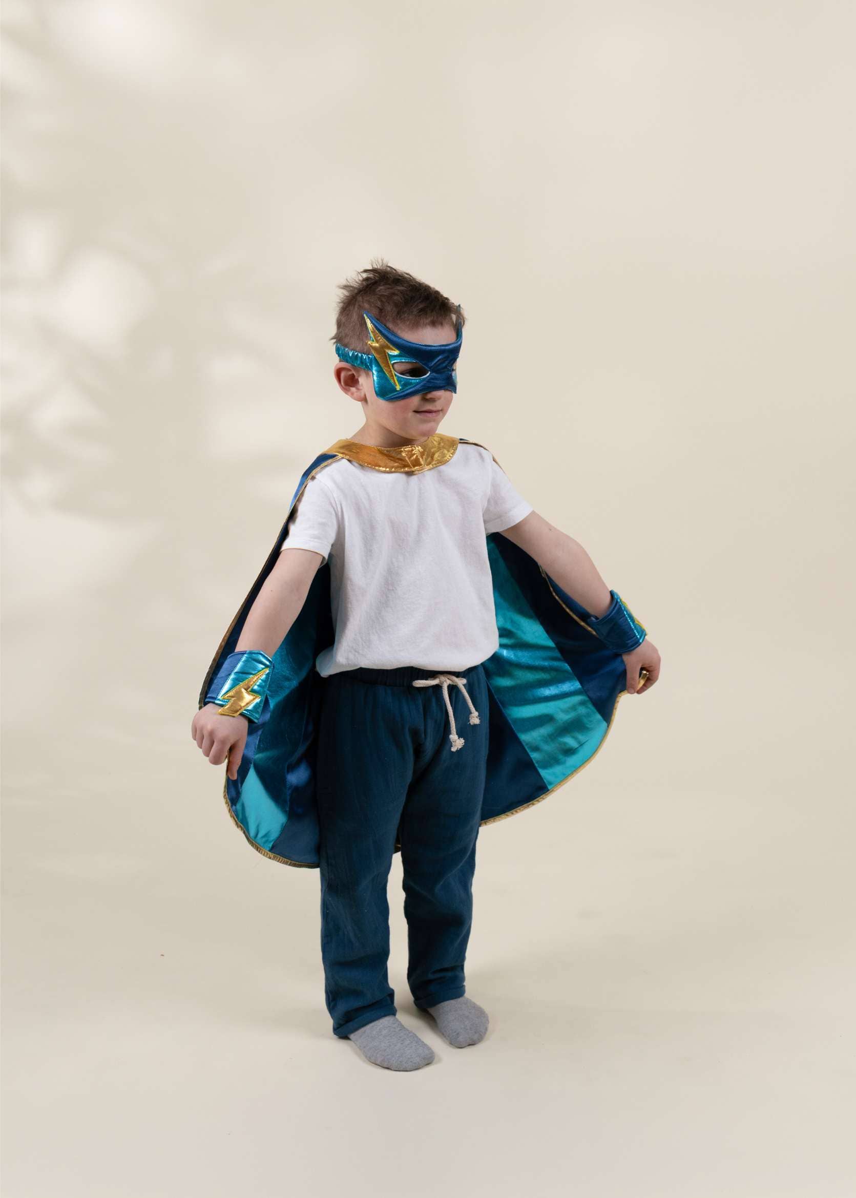 Child wearing a superhero costume with cape and mask on a plain background