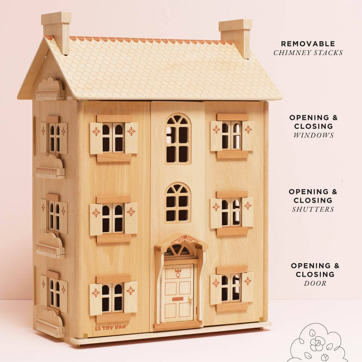 Wooden dollhouse with removable chimney stacks, opening windows, shutters, and door on a light pink background.