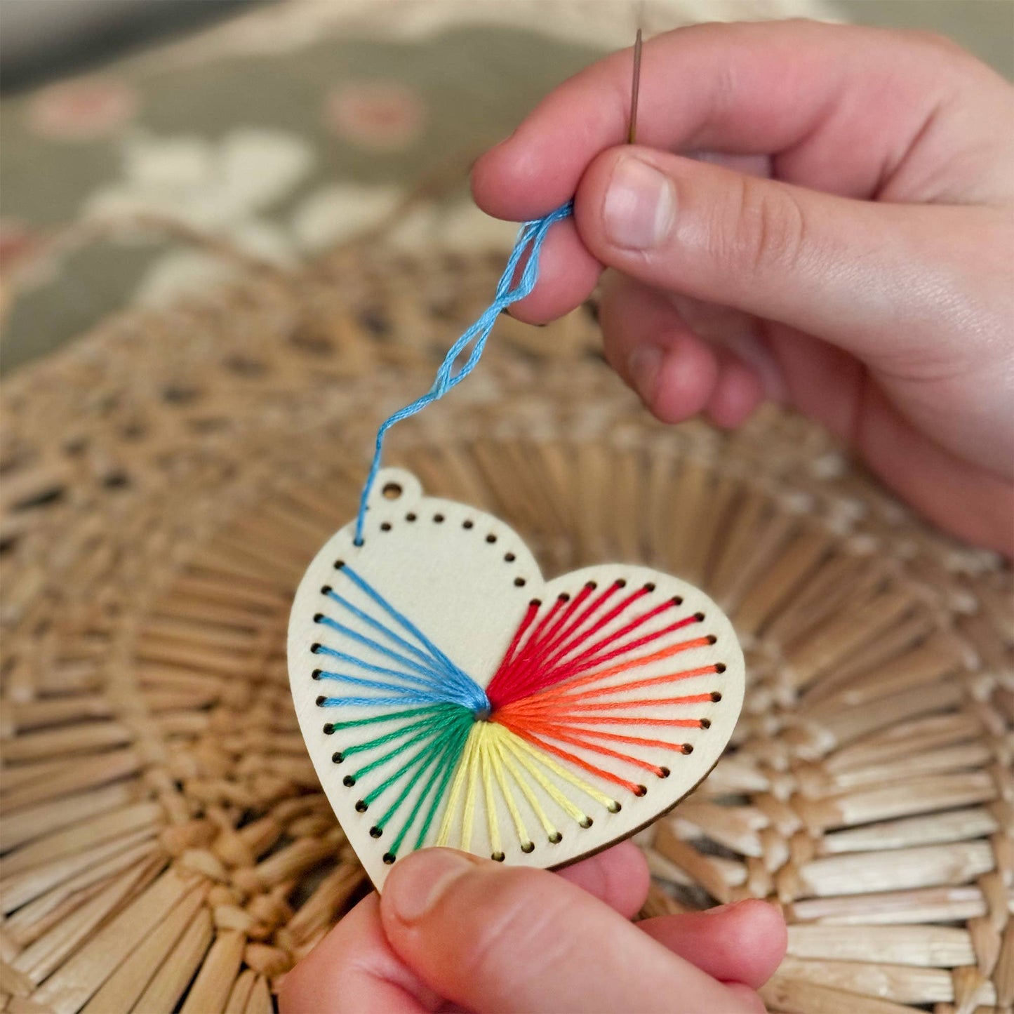 Heart-shaped colorful string art held by a hand with a woven mat background