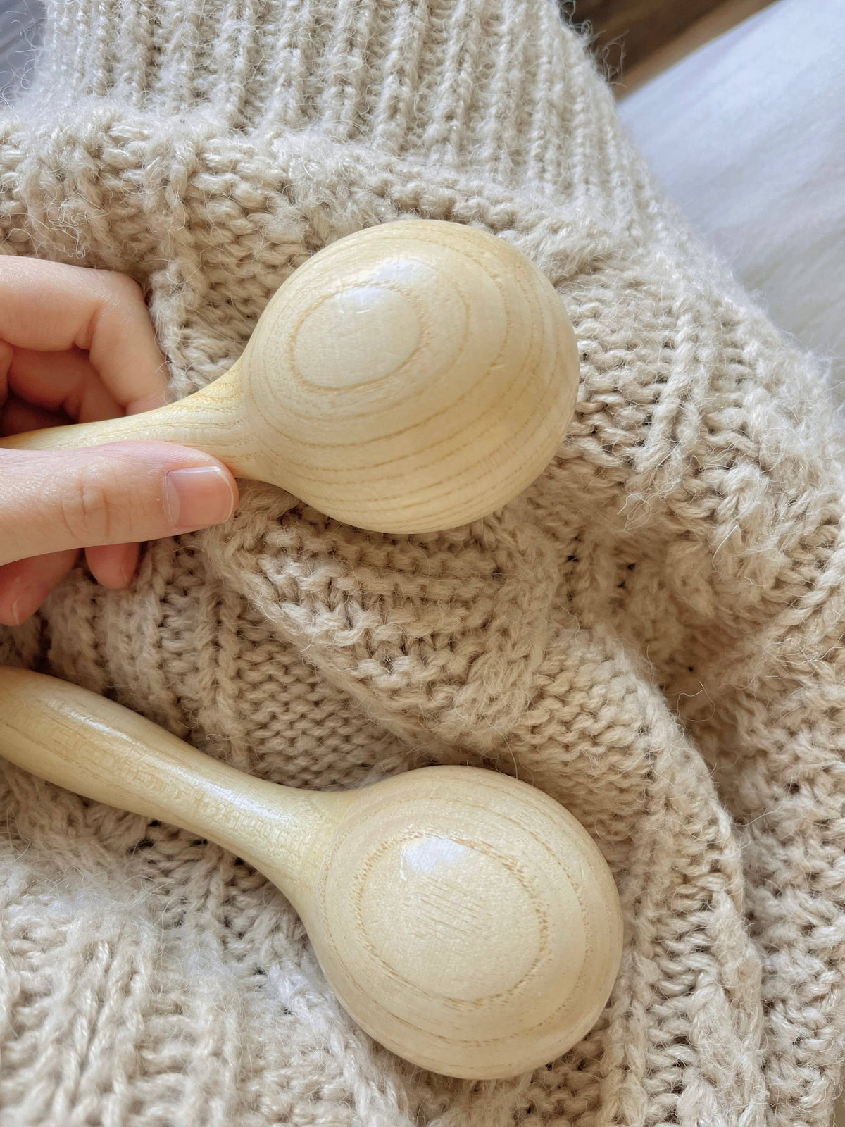 Two wooden maracas held by a hand against a textured beige fabric background