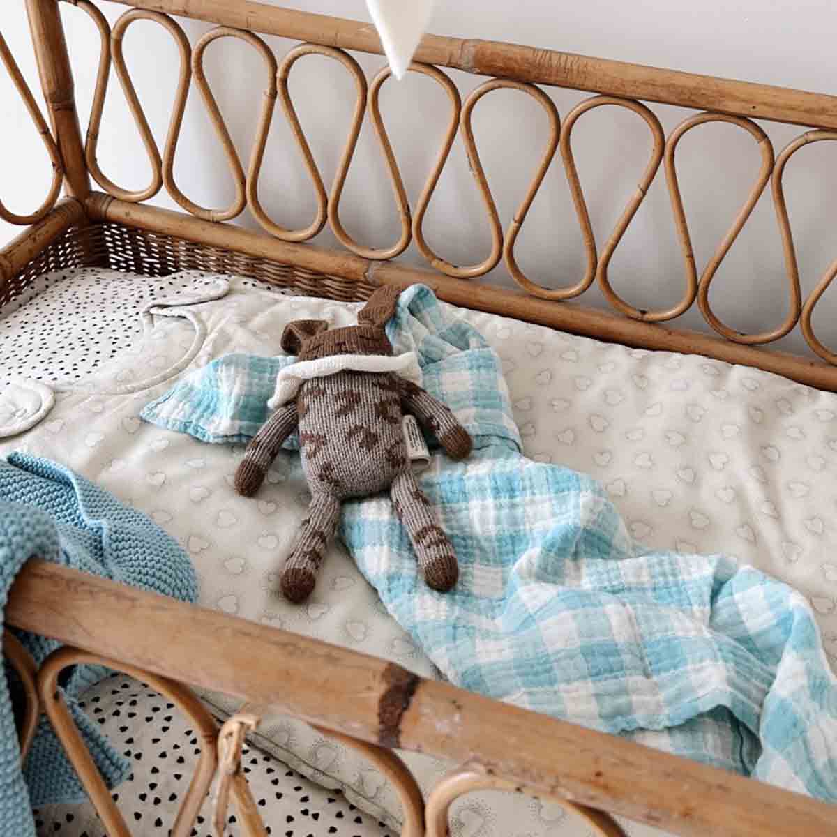 Child's bed with wicker headboard, blue checkered blanket, and stuffed animal toy.