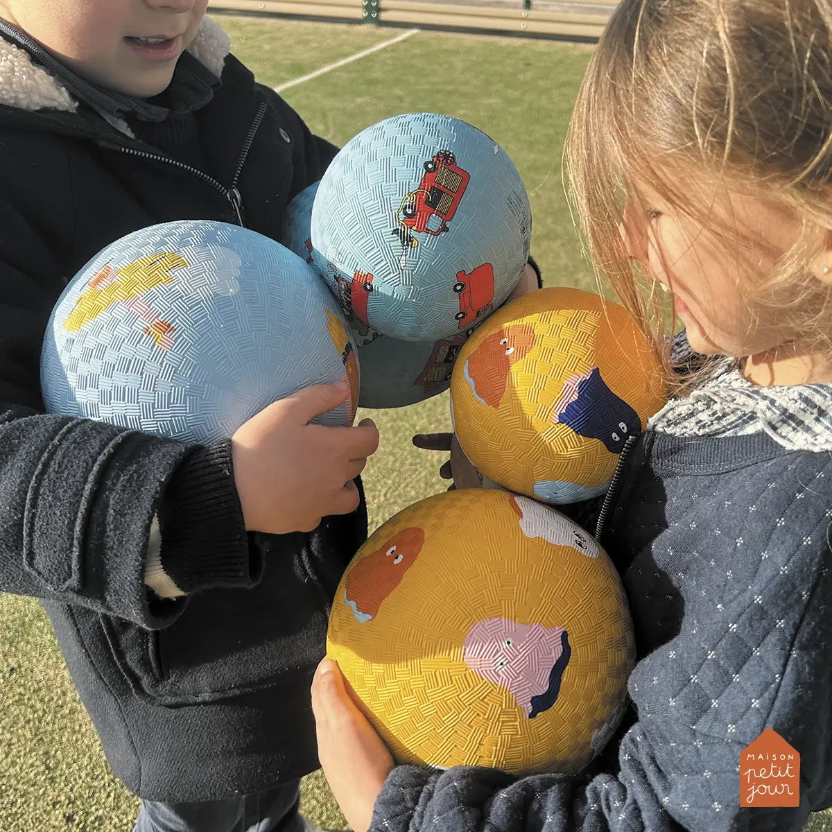Two children holding colorful bouncy balls with world map designs outdoors.