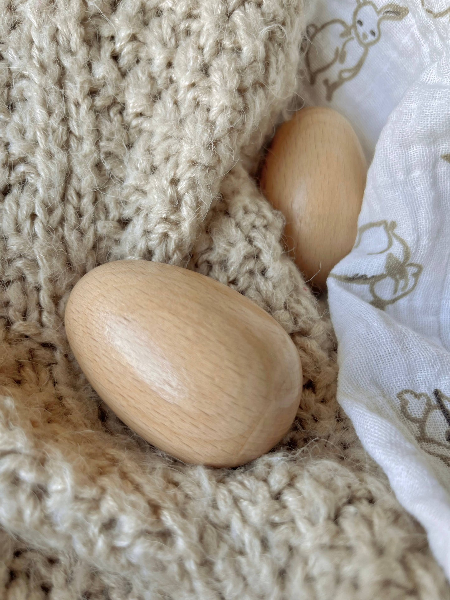 Two wooden eggs on a textured beige fabric surface.