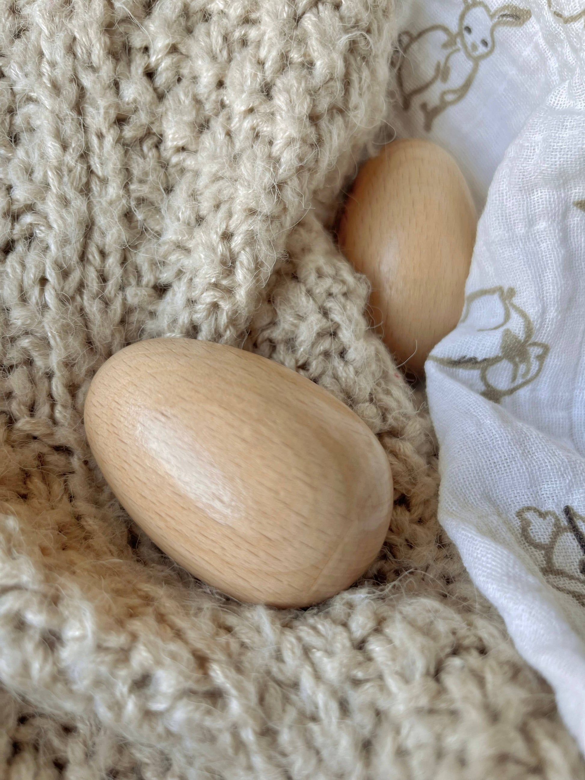 Two wooden eggs on a textured beige fabric surface.