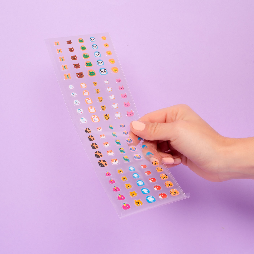 Hand holding a clear sheet with colorful emoji stickers against a purple background