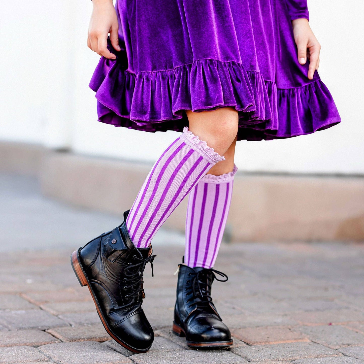 Person wearing a purple dress, striped socks, and black shoes on a blurred background