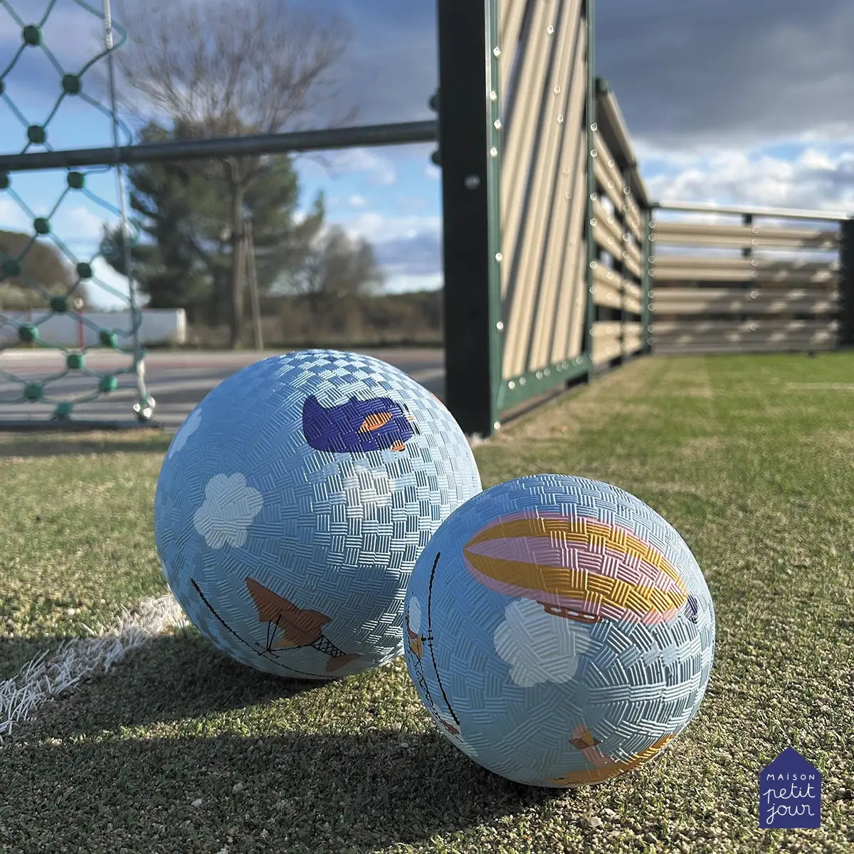 Two children's bouncy balls with airplane designs on a grassy field.