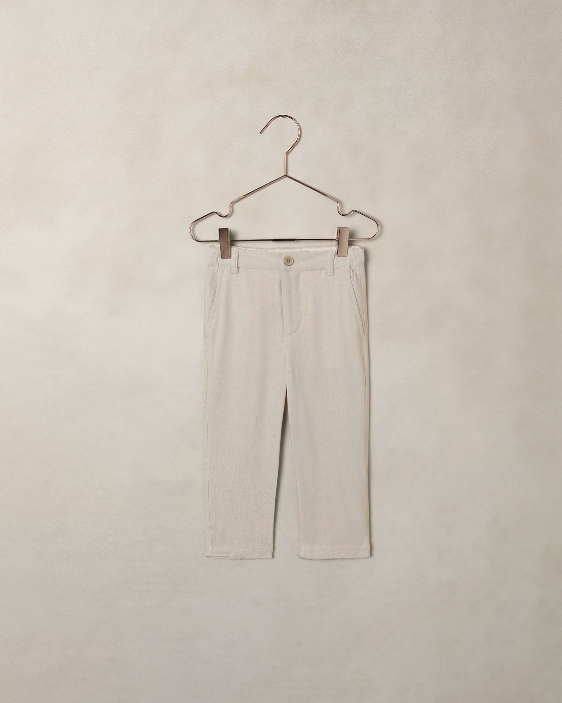 Beige dress pants on a hanger against a beige wall