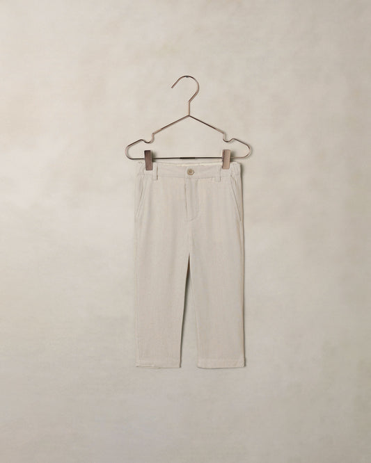 Beige dress pants on a hanger against a beige wall