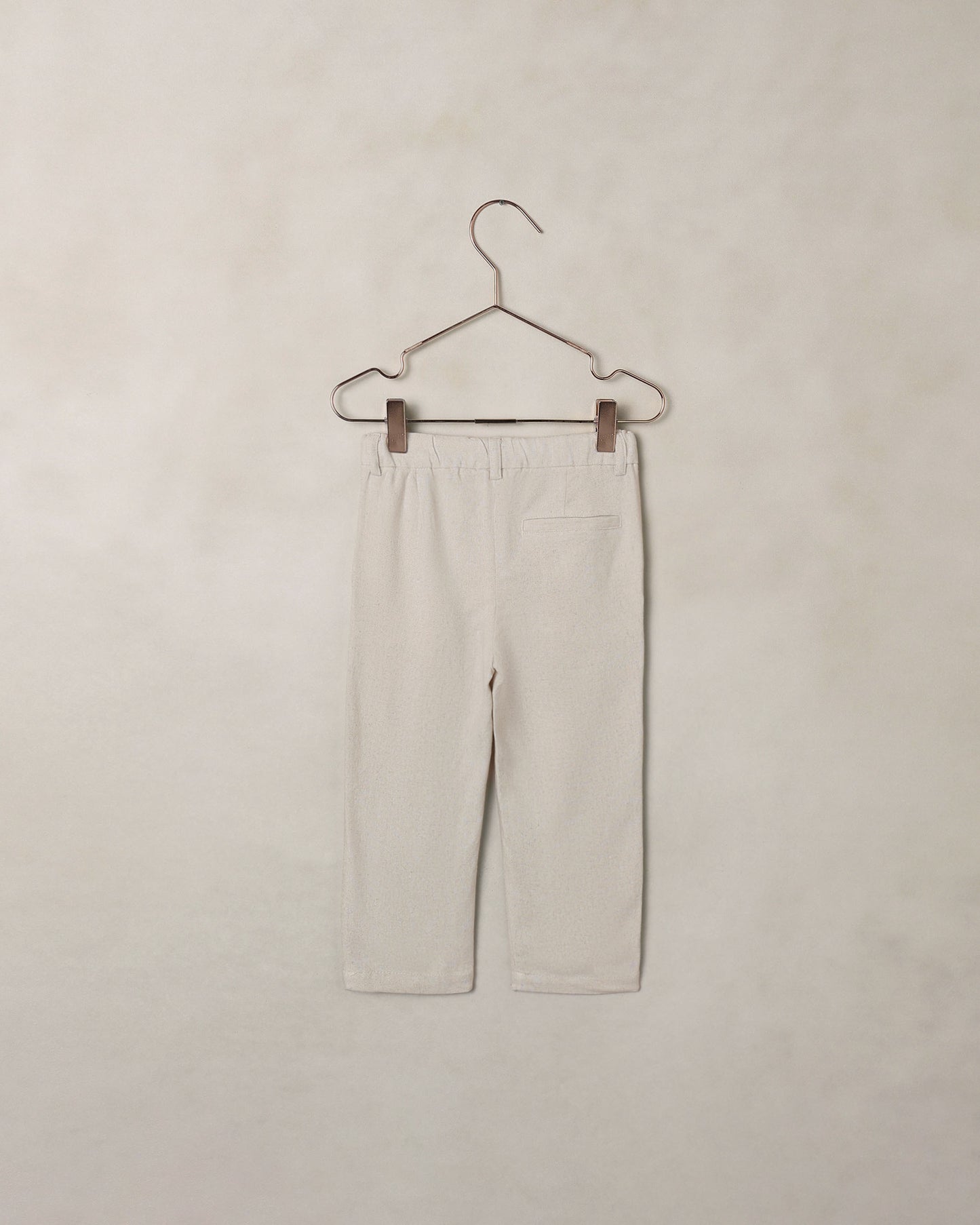 Back of beige dress pants on a hanger against a beige background