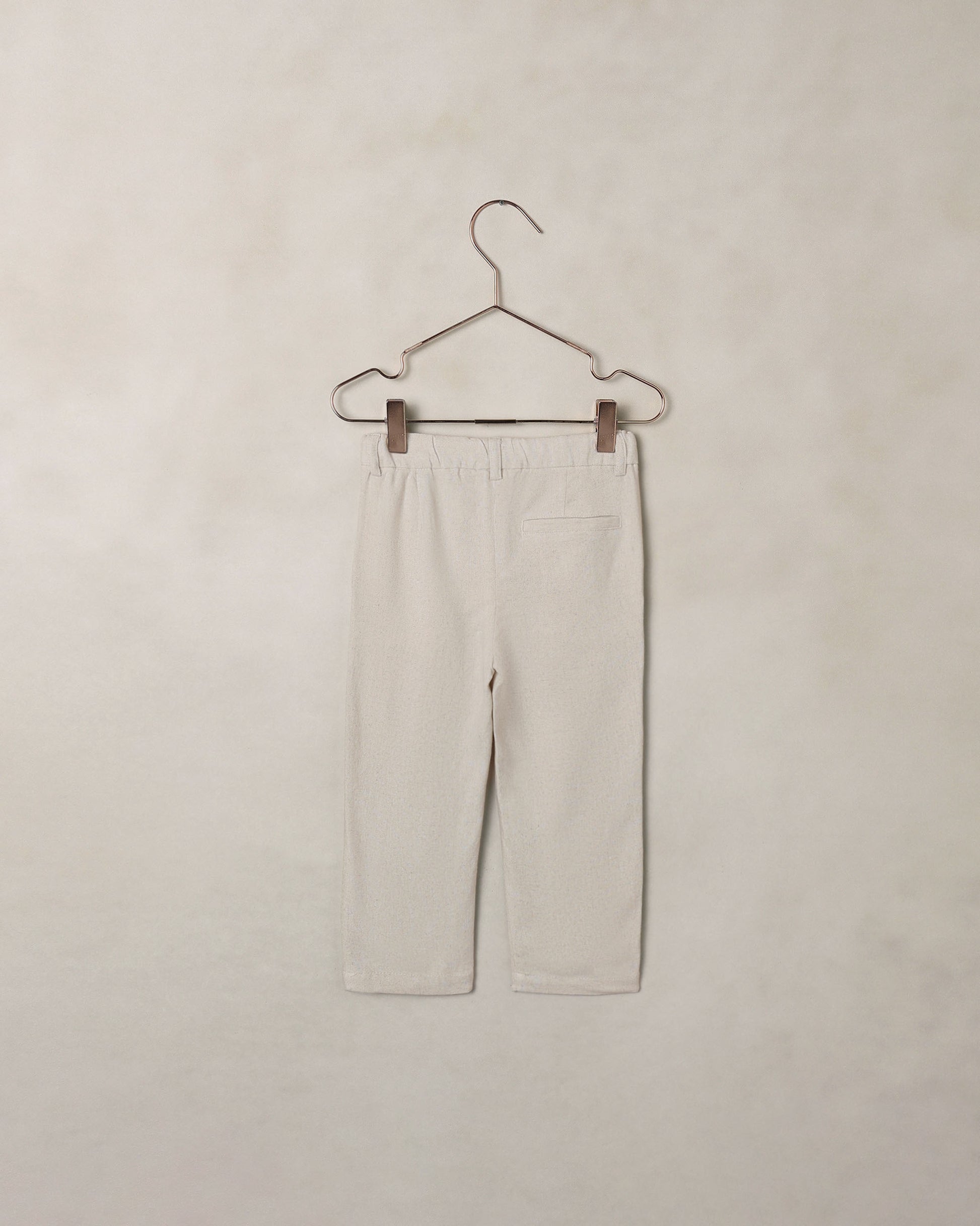 Back of beige dress pants on a hanger against a beige background