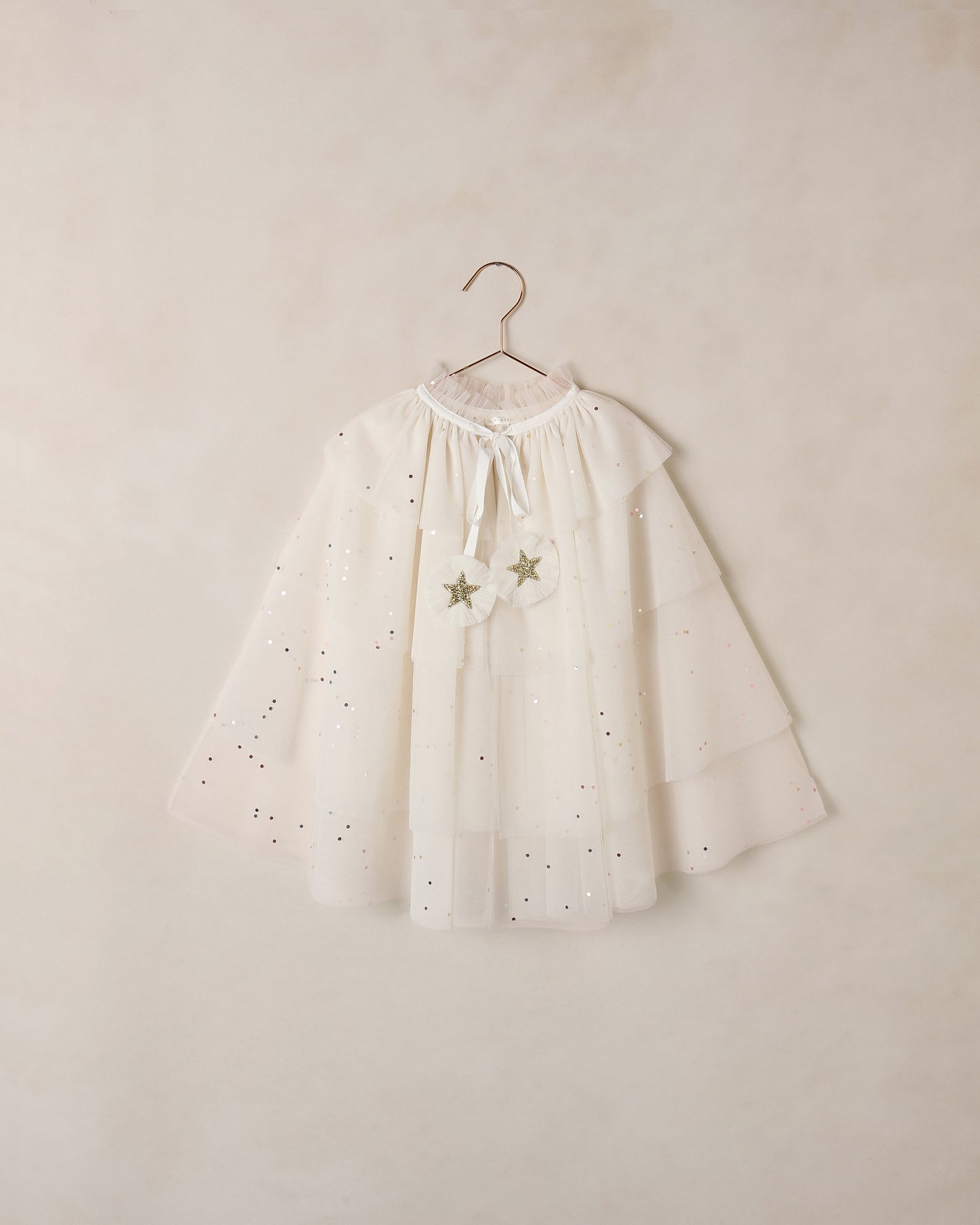 White tulle cape with star details on a hanger against a beige wall