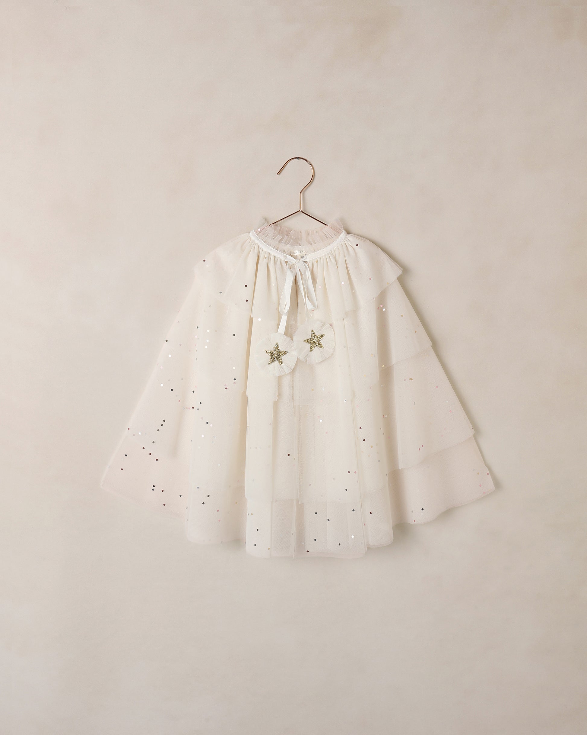 White tulle cape with star details on a hanger against a beige wall