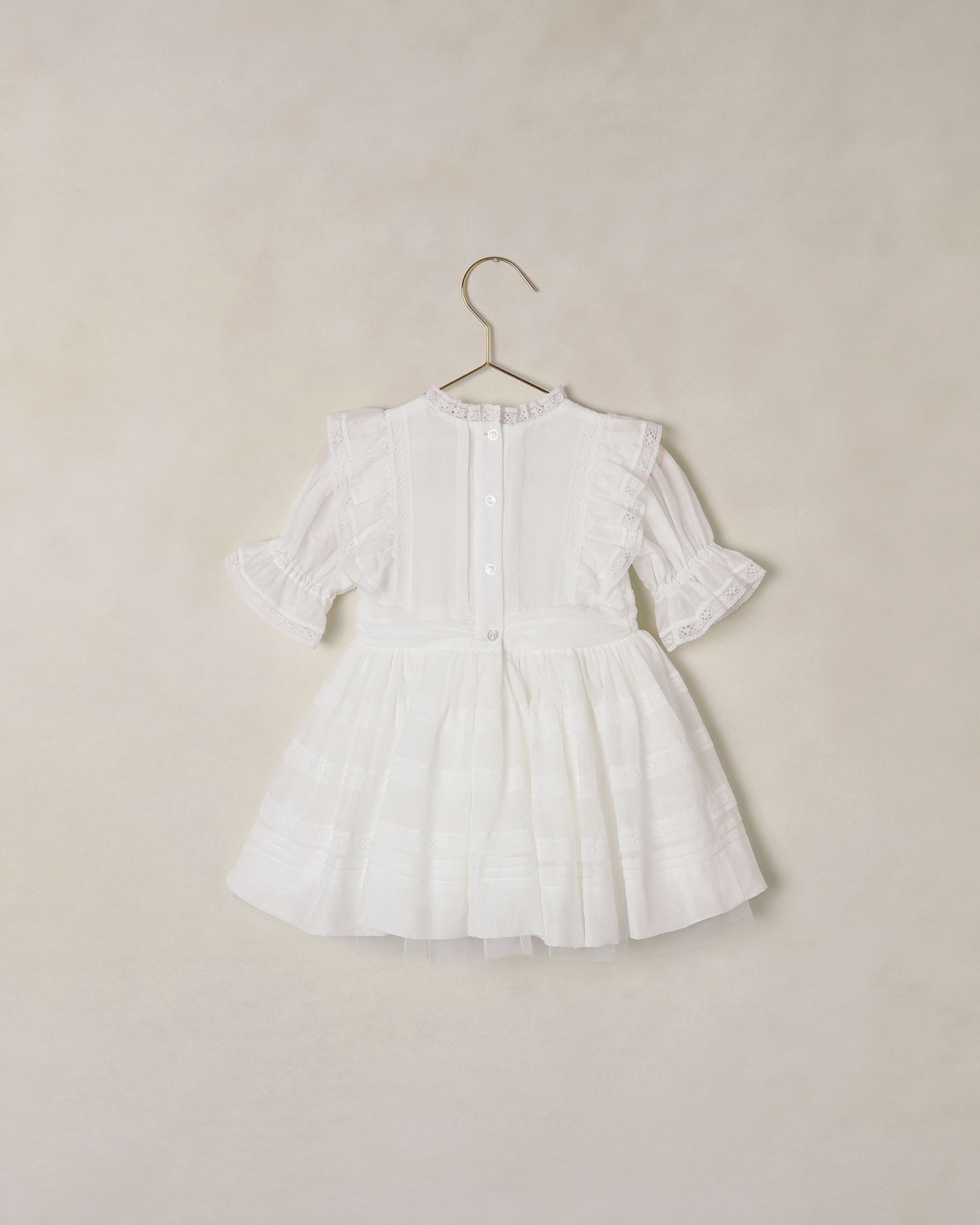 Back of white dress on a hanger against a beige background