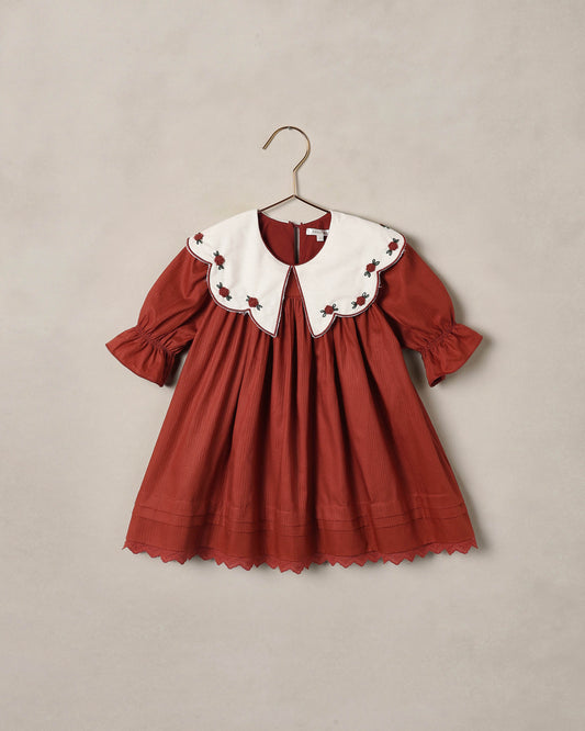 Ruby red children's dress with large white scalloped collar and pleated skirt, shown on a beige backdrop