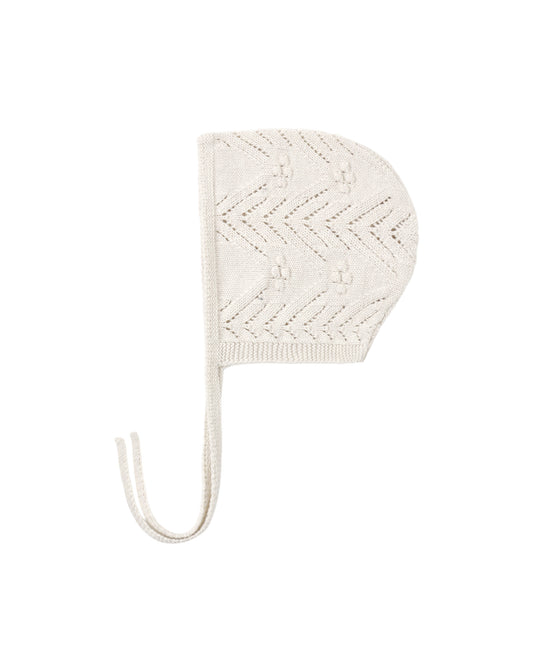 Knitted baby bonnet in oatmeal color, shown on a white background
