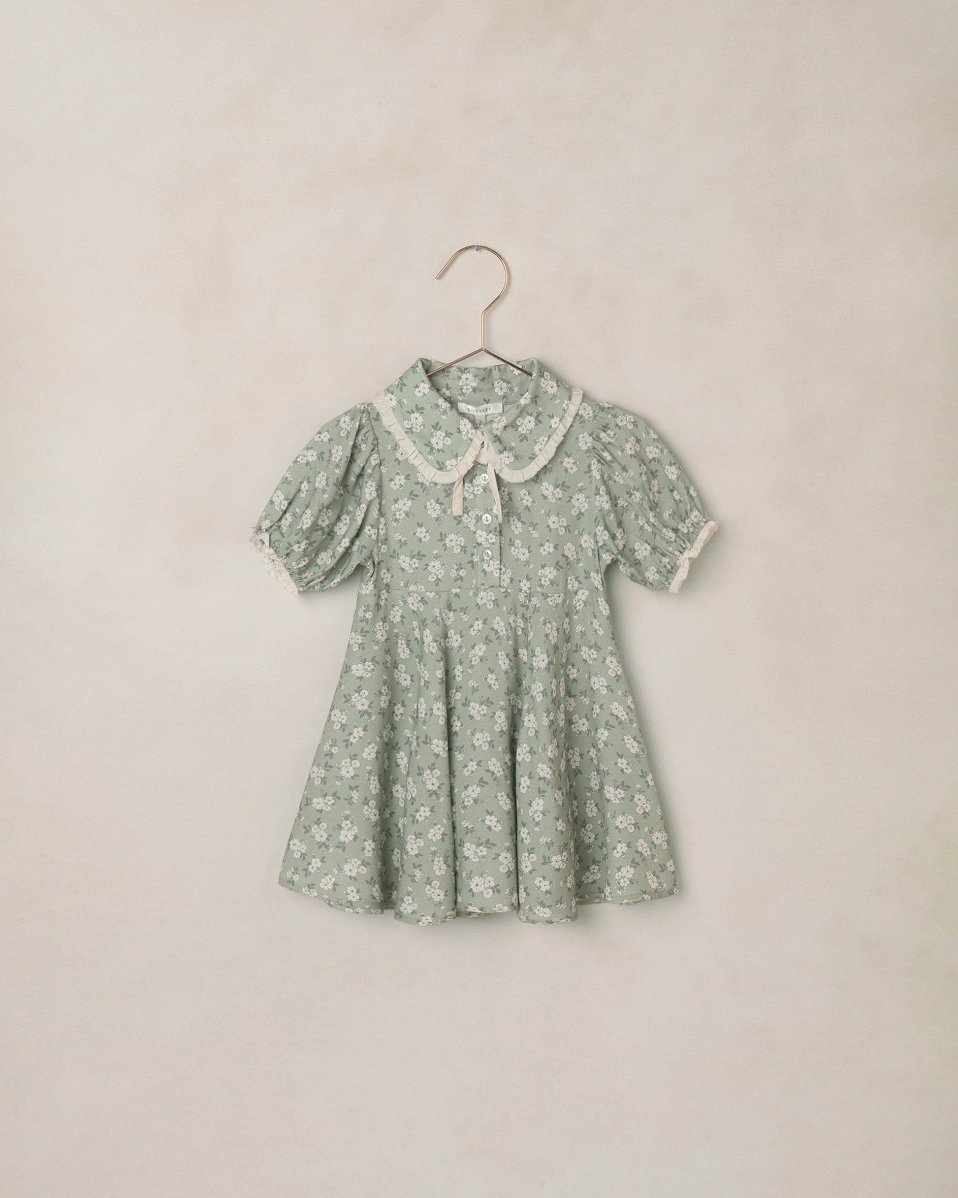 Green floral dress on a hanger against a beige background