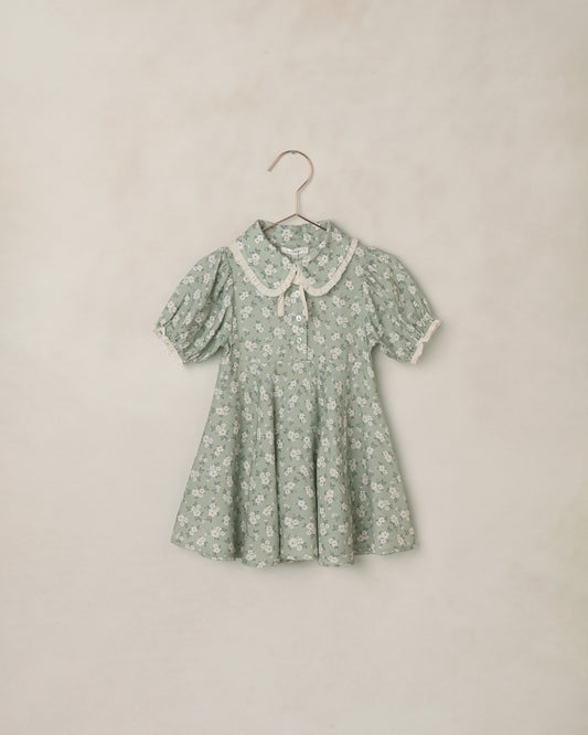 Green floral dress on a hanger against a beige background