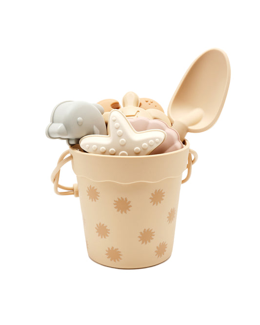 Beige silicone beach bucket with sun design and beach toys inside on a white background