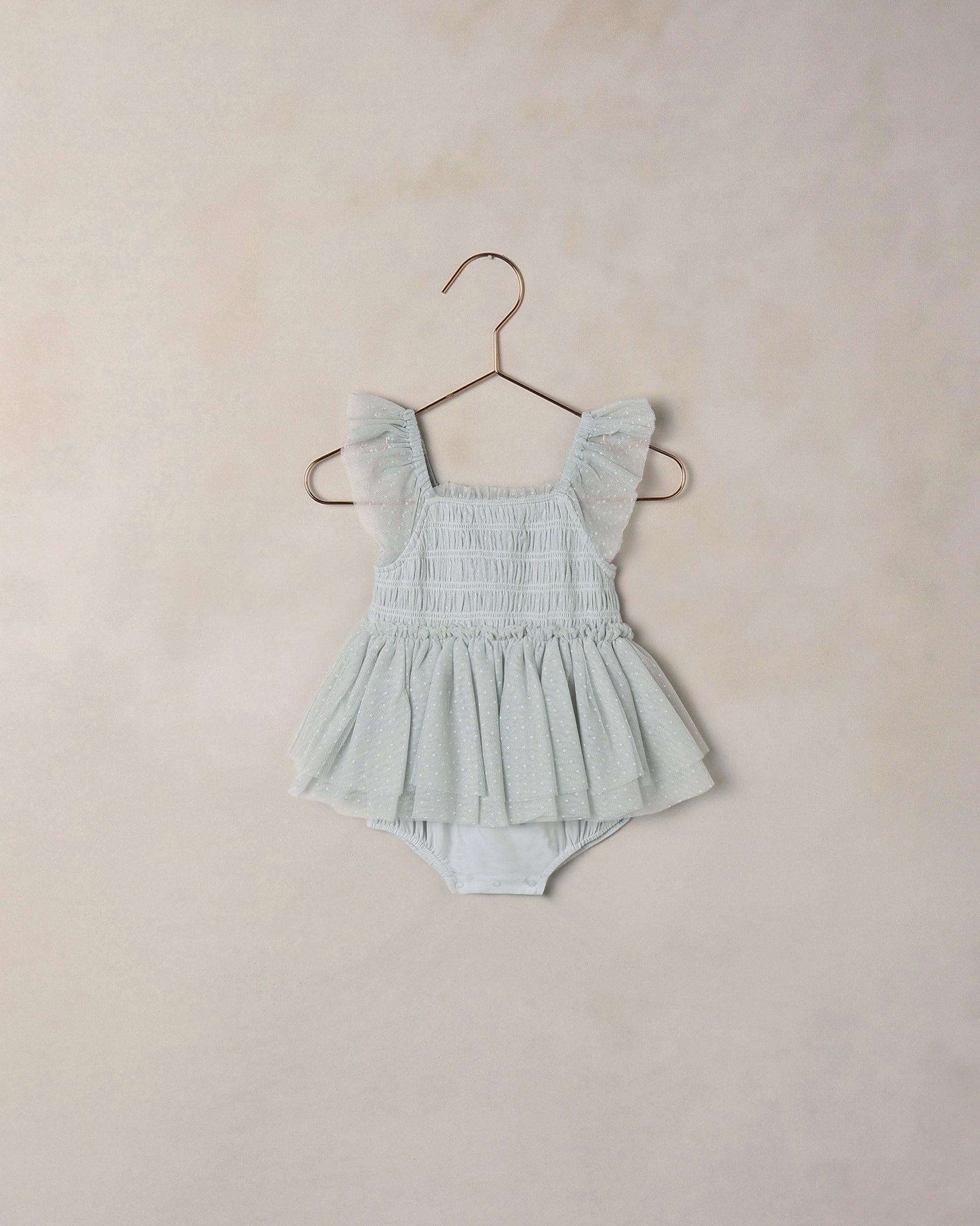 Light blue baby romper with ruffled straps on a beige background