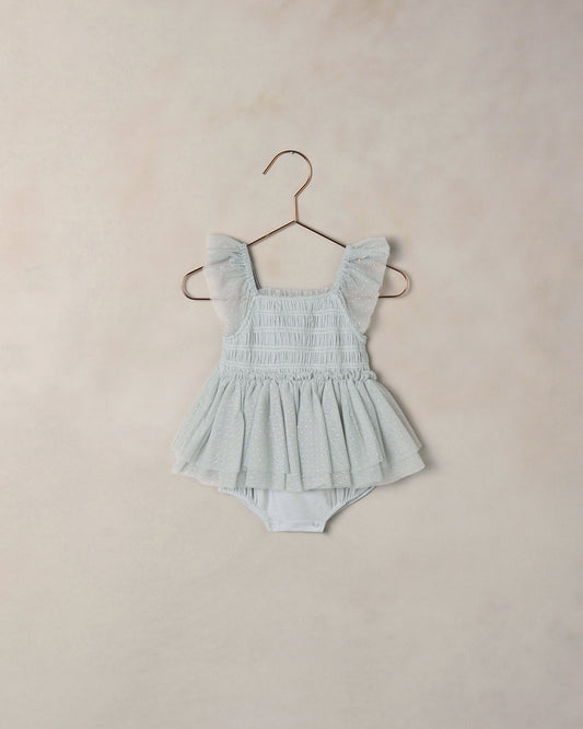 Light blue baby romper with ruffled straps on a beige background