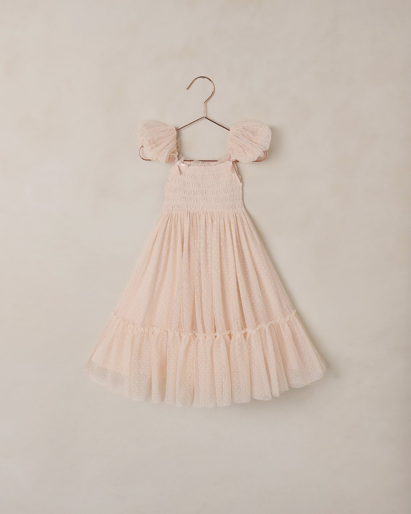 Blush pink dress with ruffled sleeves on a hanger against a beige background