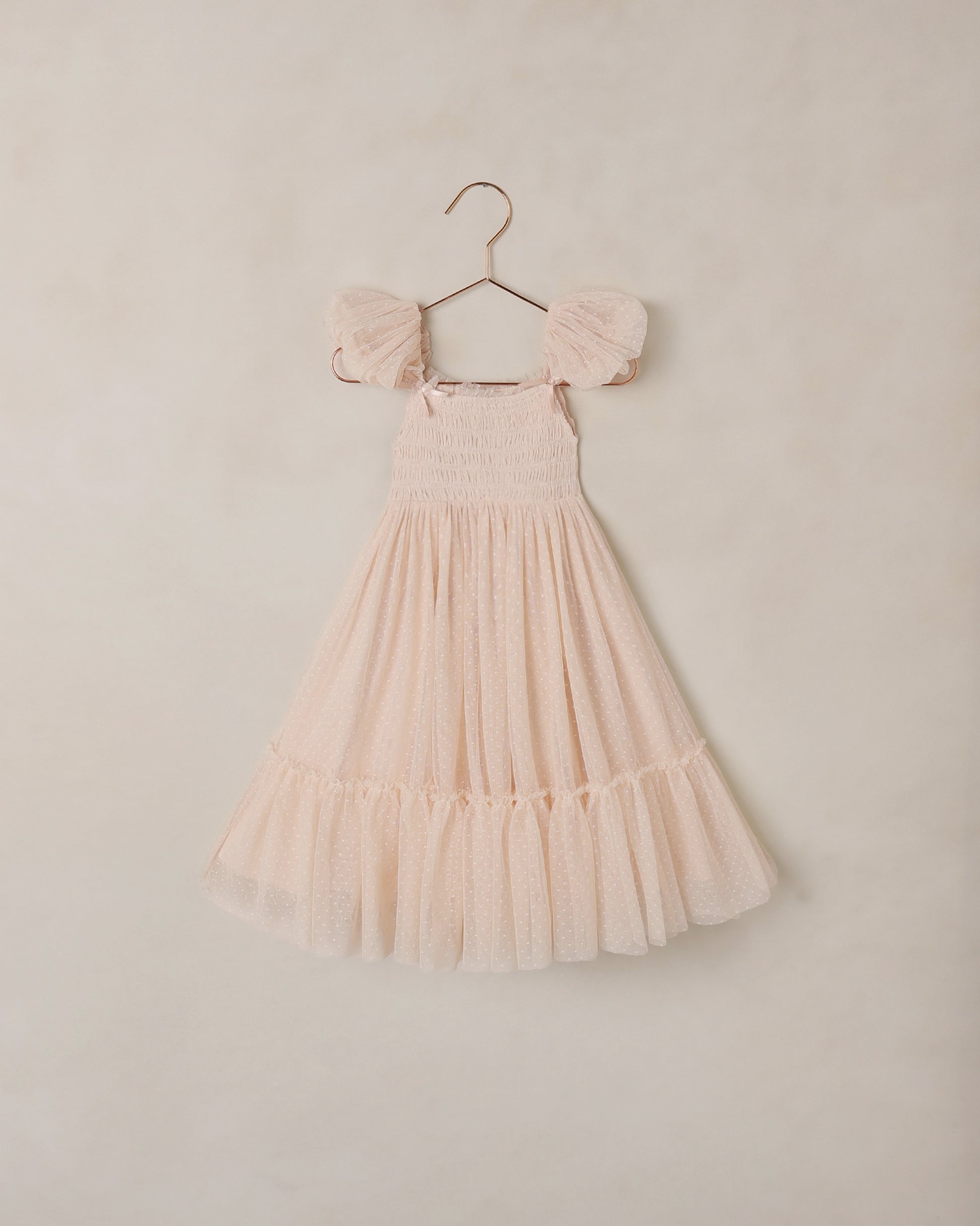 Blush pink dress with ruffled sleeves on a hanger against a beige background