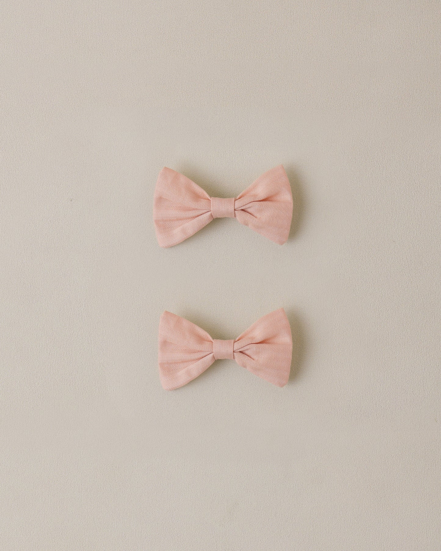 two pink bow hair clips on a beige background