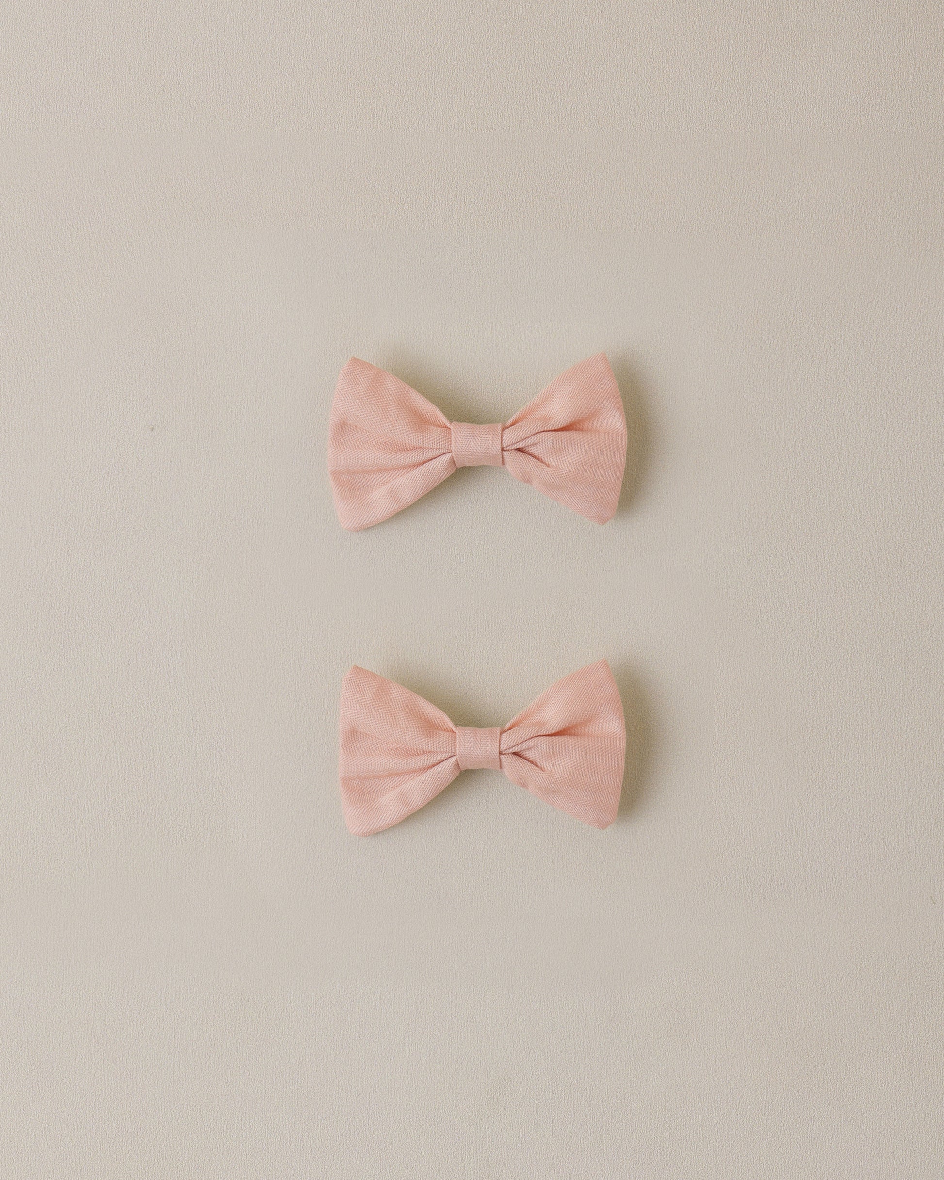 two pink bow hair clips on a beige background