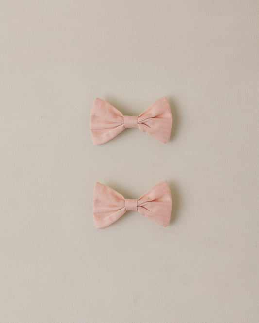 two pink bow hair clips on a beige background