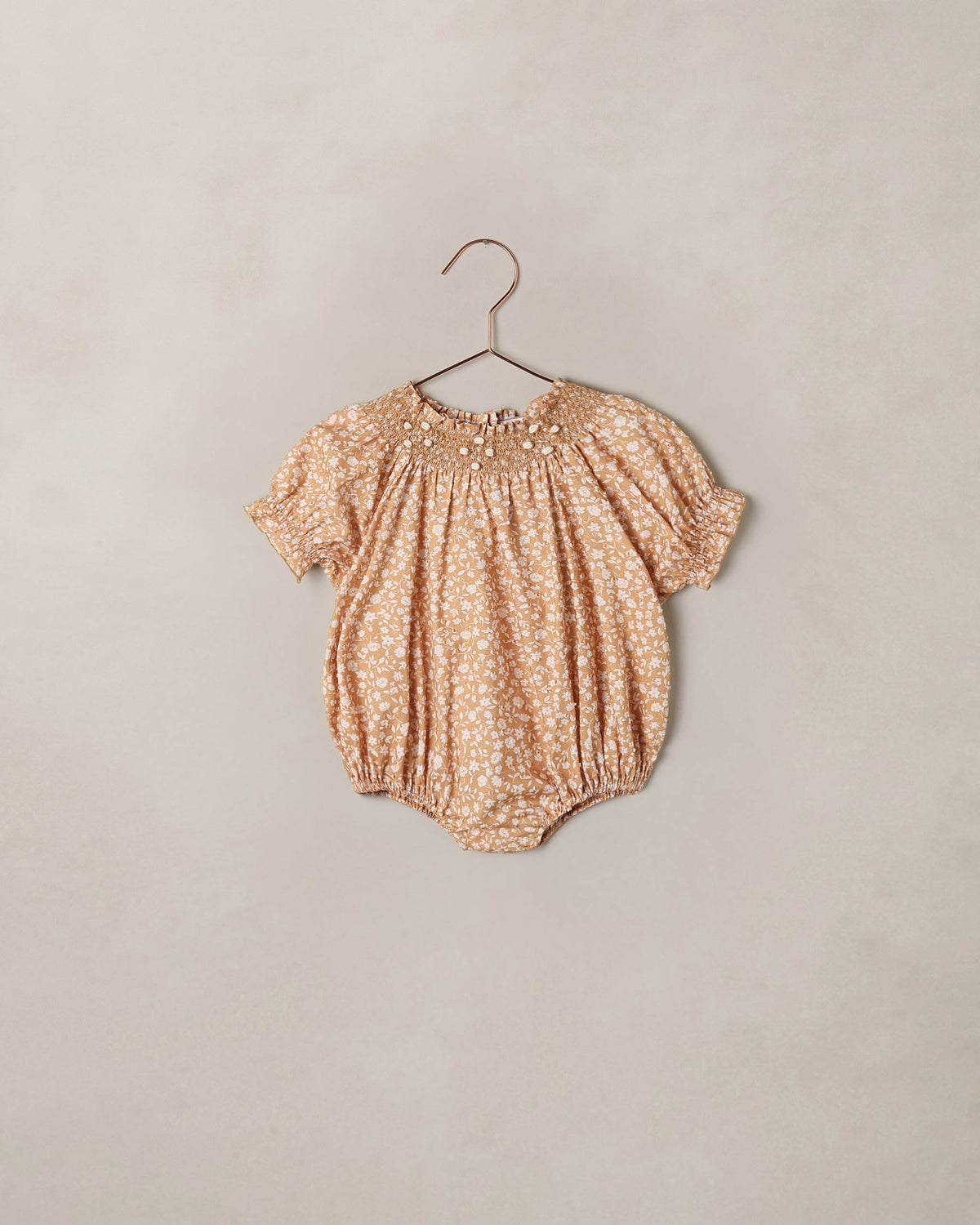 Baby romper with floral pattern on a hanger against a beige background