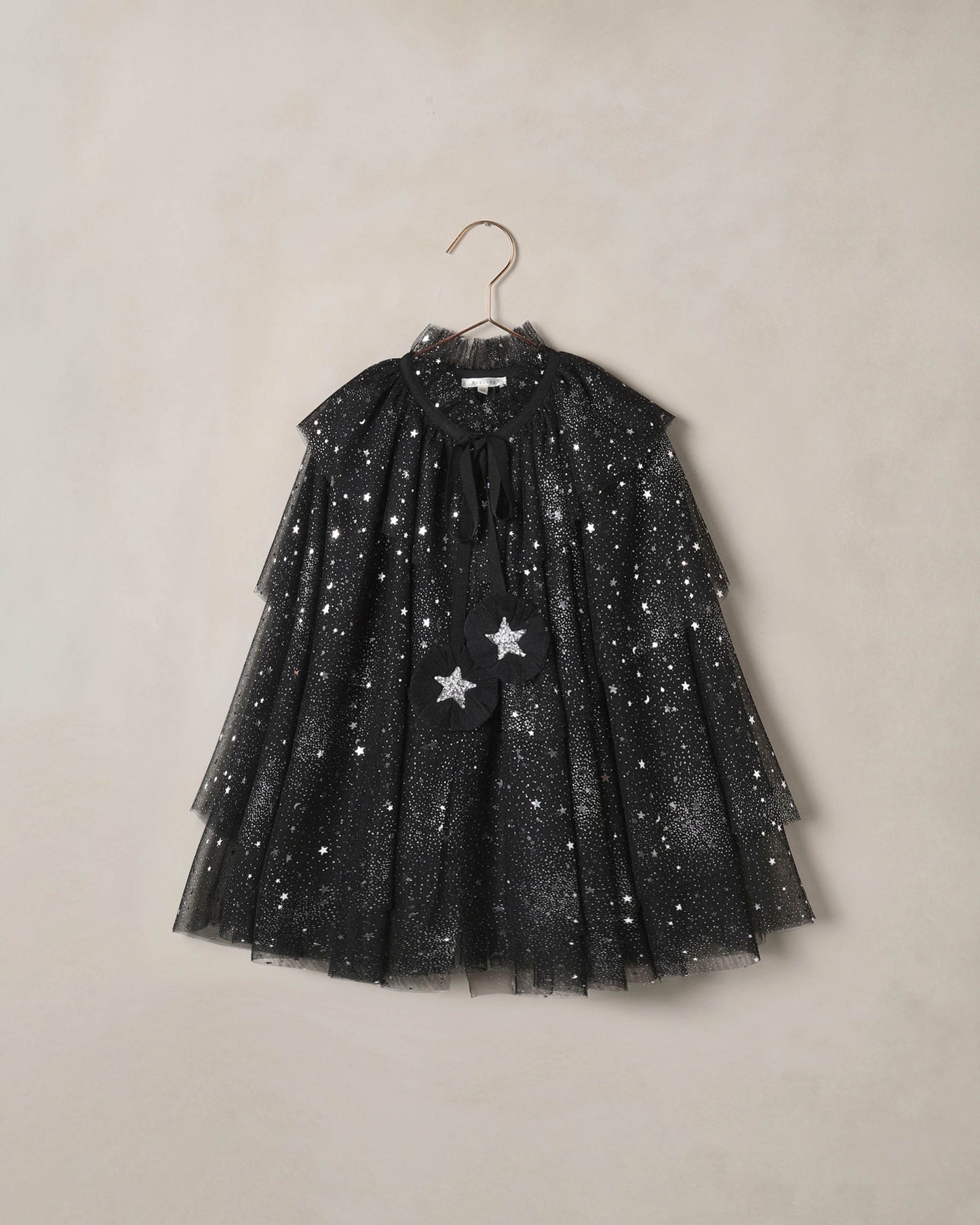 Black tulle cape for children with silver starts on it, on a beige background
