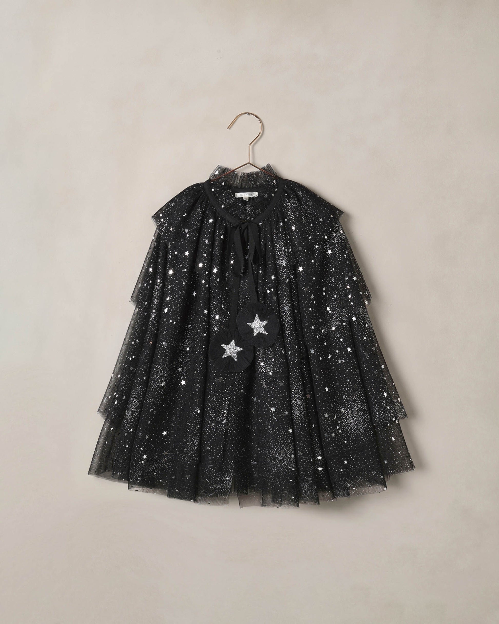 Black tulle cape for children with silver starts on it, on a beige background