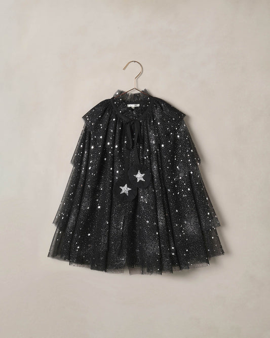 Black tulle cape for children with silver starts on it, on a beige background