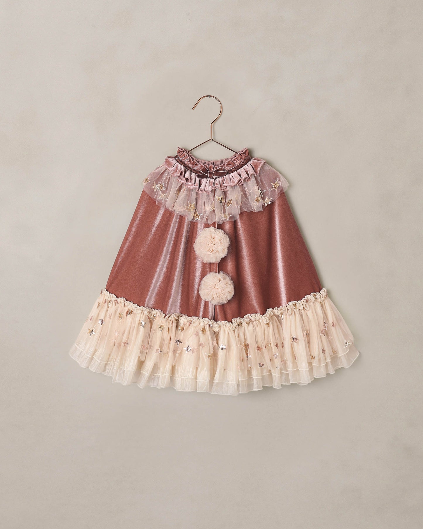 dark pink clown cape with ivory ruffles and pom poms on a beige background