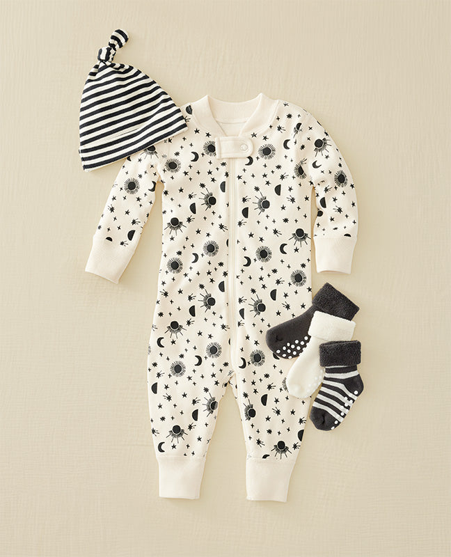Baby onesie with black patterns, striped hat, and socks on a beige background
