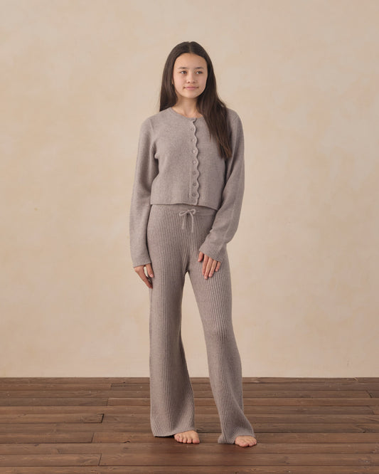 Woman wearing a gray knit outfit standing on a wooden floor with a beige wall background