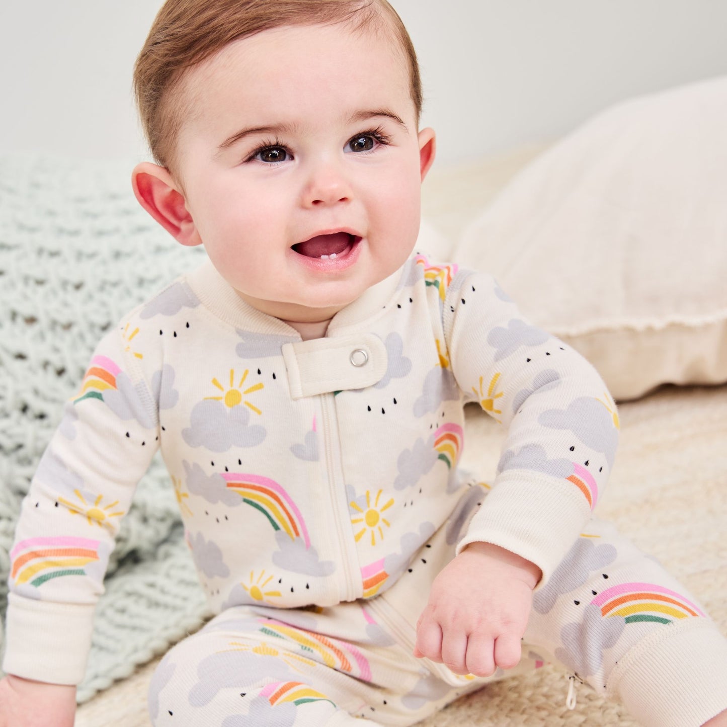 Baby wearing a onesie with rainbow and cloud patterns on a neutral background