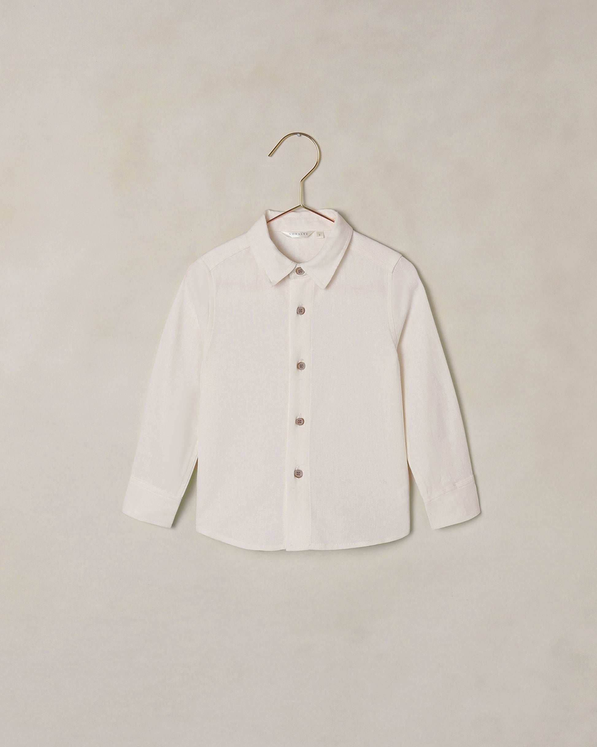 White button down collared shirt on a hanger against a beige background