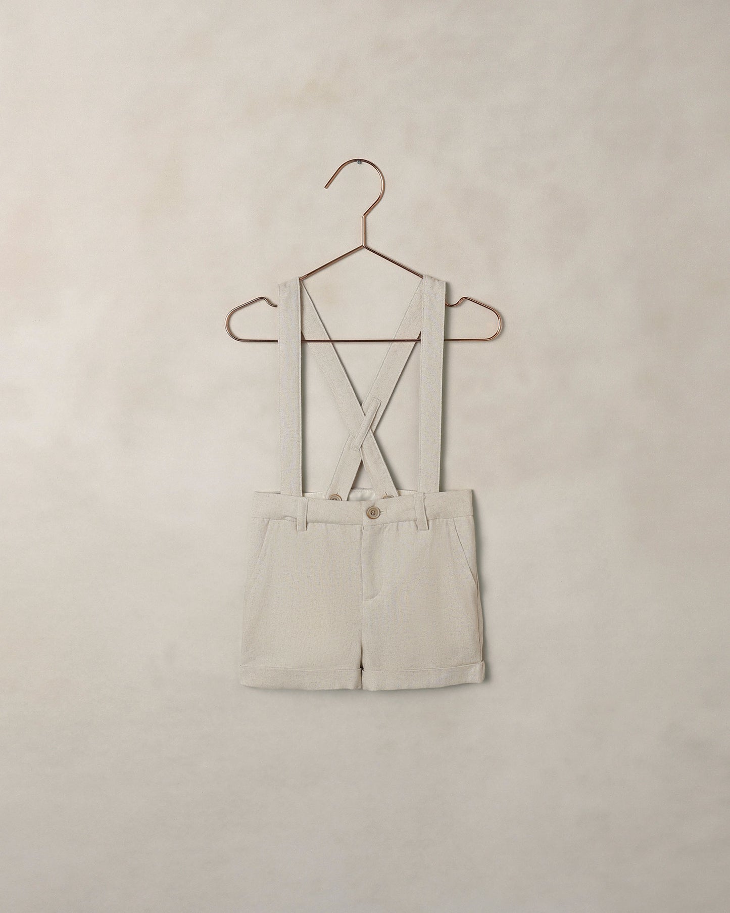 Beige shorts overalls on a hanger against a beige wall