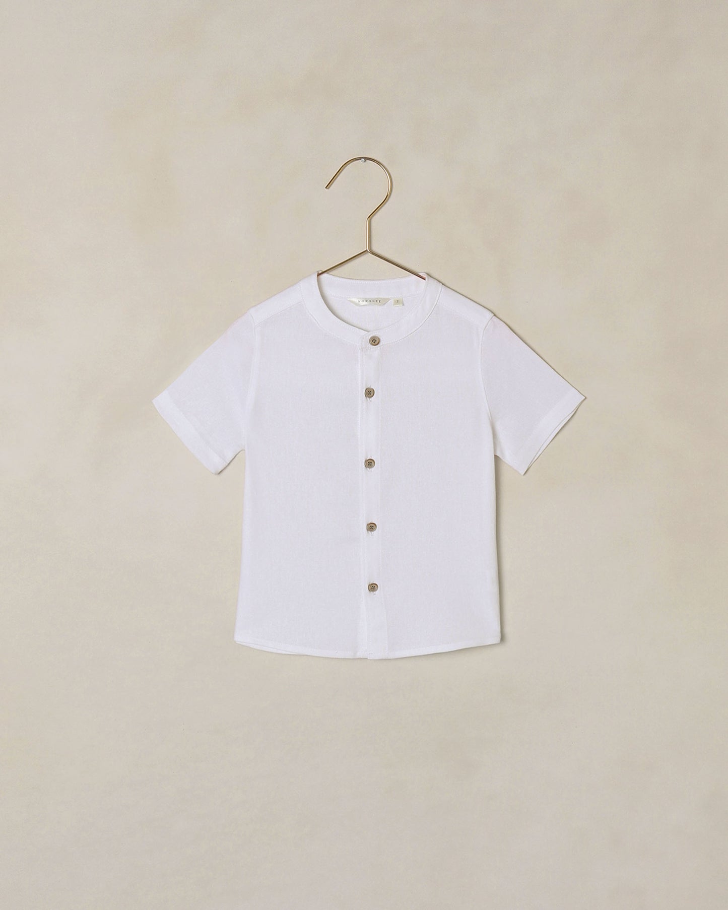 White button-down collarless shirt on a hanger against a beige background