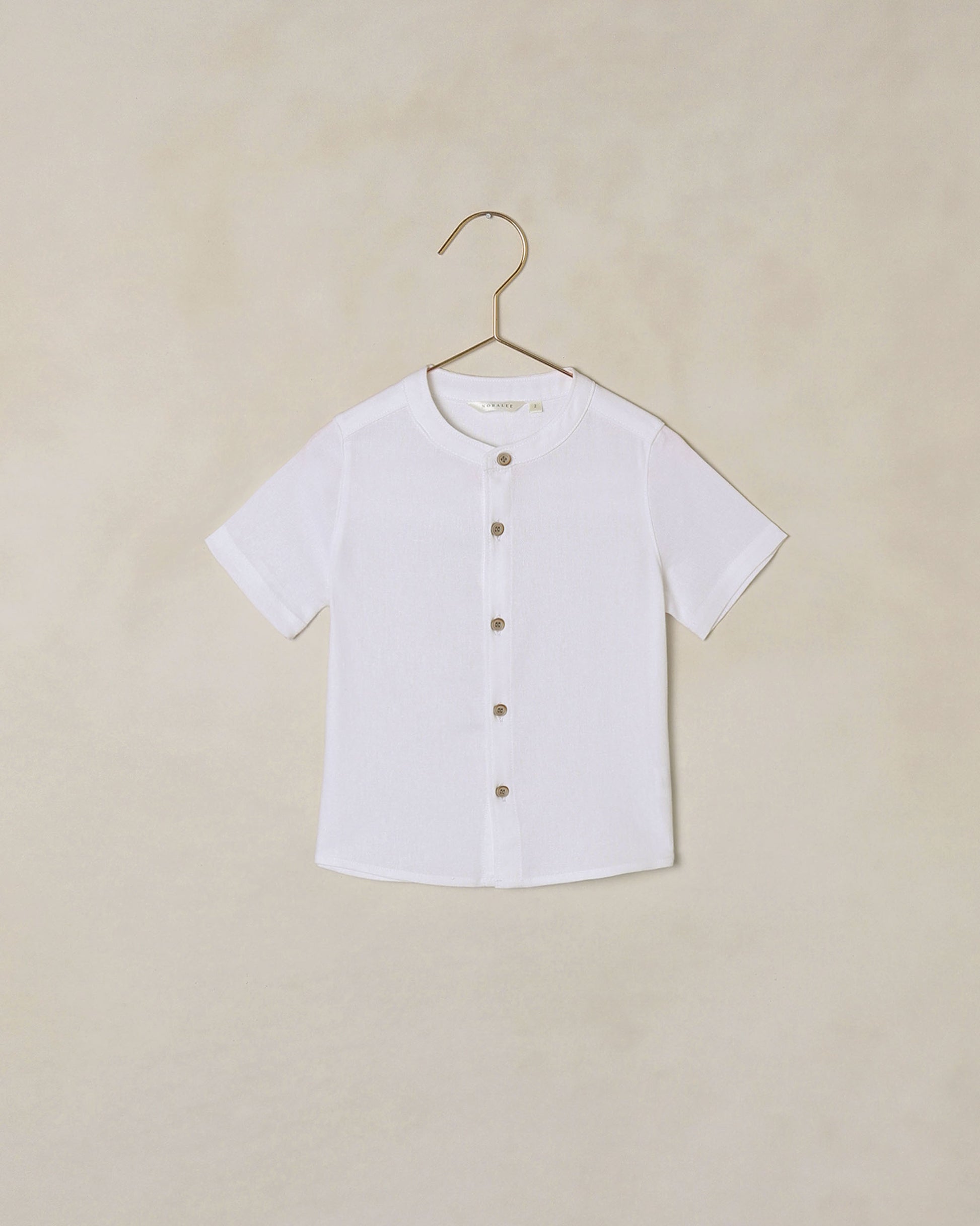 White button-down collarless shirt on a hanger against a beige background