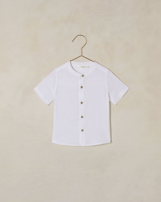 White button-down collarless shirt on a hanger against a beige background