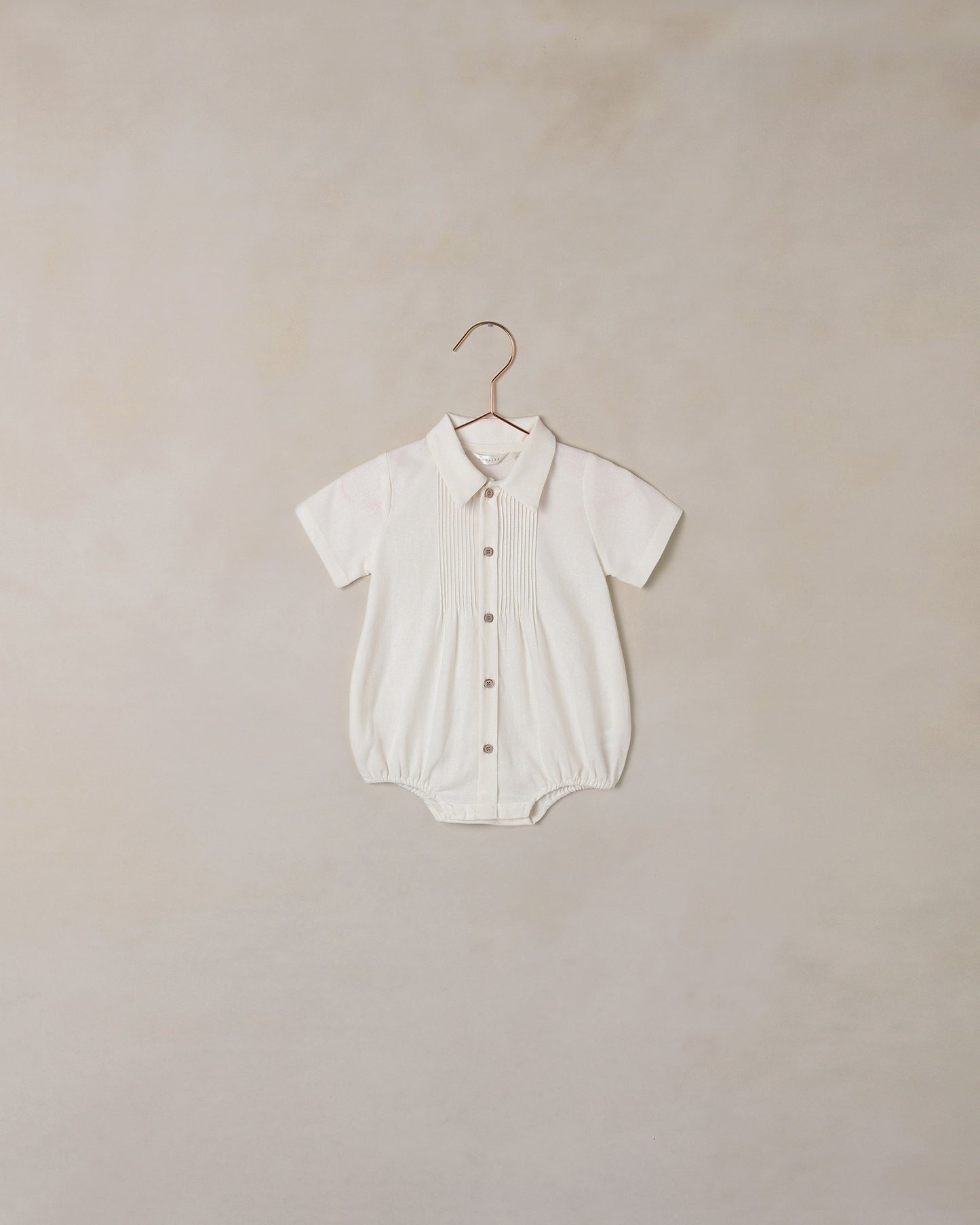 White baby romper on a hanger against a beige background