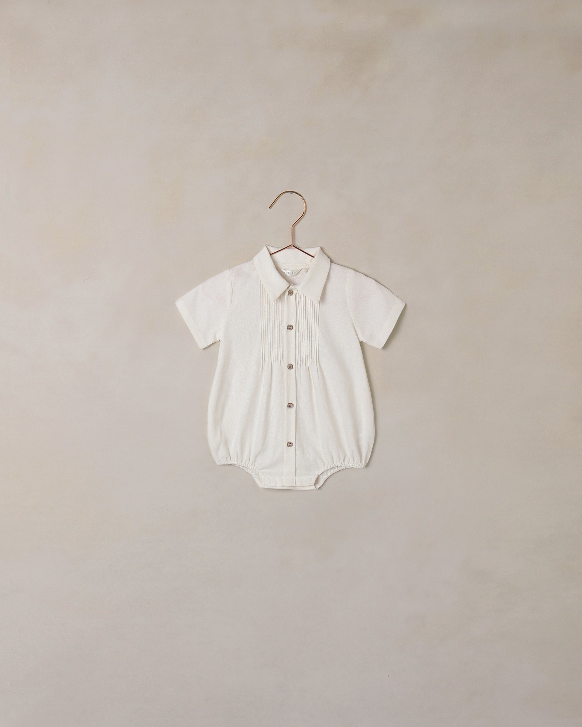 White baby romper on a hanger against a beige background